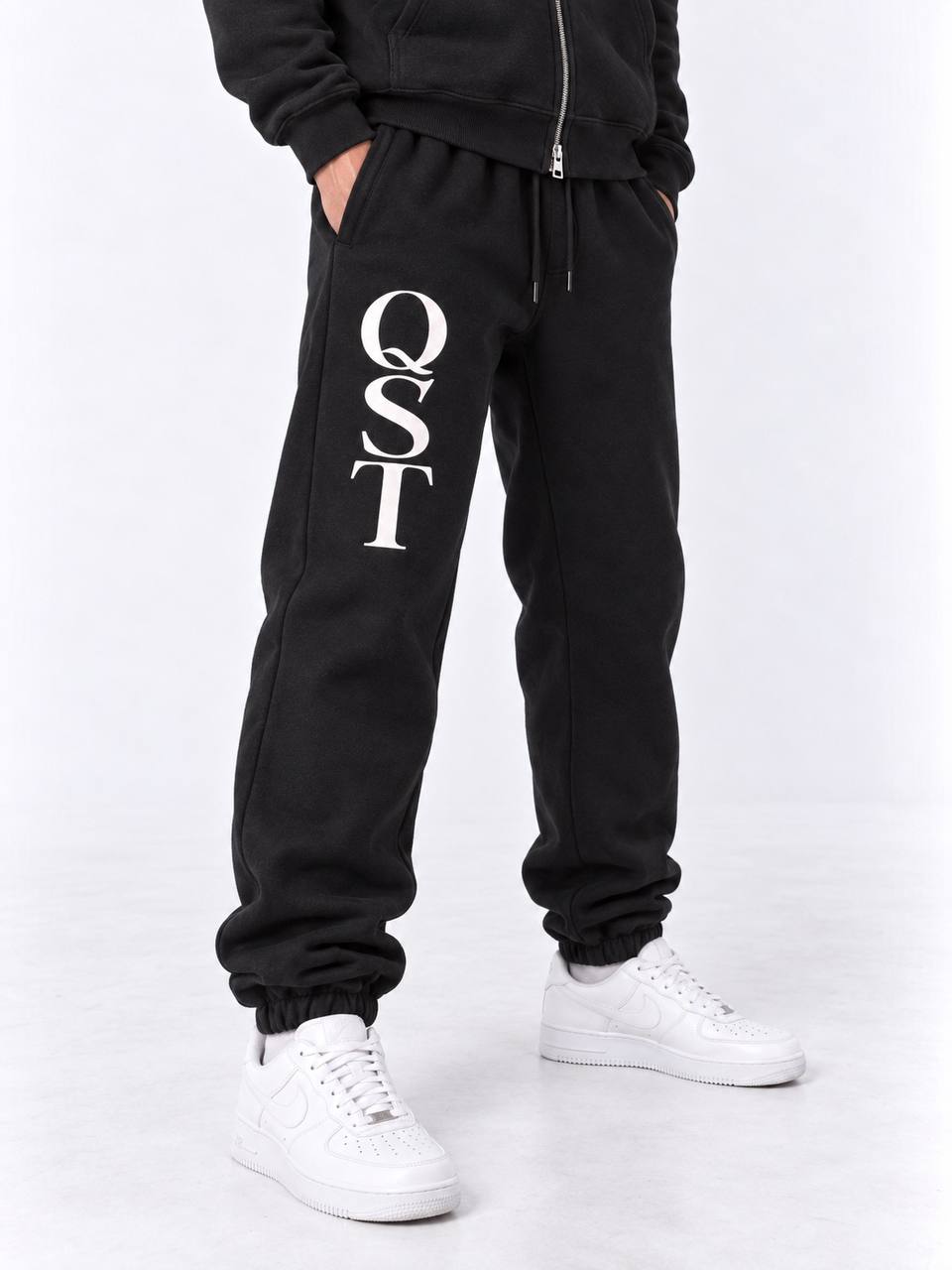 Black cuffed joggers with stacked white QST serif monogram on the thigh