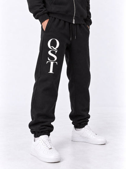 Black cuffed joggers with stacked white QST serif monogram on the thigh