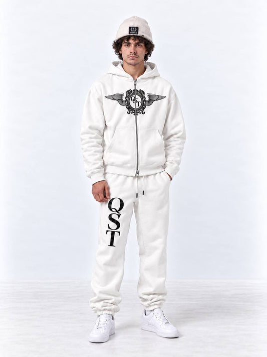 A man modeling a white zip-up hoodie and matching sweatpants set. The hoodie features a black winged crest graphic on the chest, and the sweatpants have 'QST' printed vertically in black on the left leg.