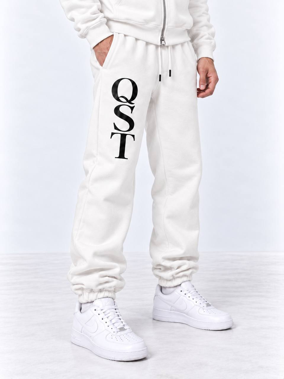 Black cuffed joggers with stacked white QST serif monogram on the thigh