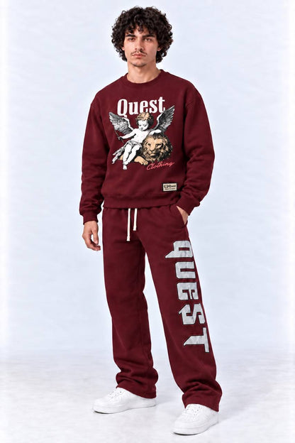A man modeling a matching burgundy sweatshirt and sweatpants set from the brand Quest. The sweatshirt features a graphic of a cherub and lion with 'Quest' printed in white, and the sweatpants have 'QUEST' printed vertically in white down the left leg.